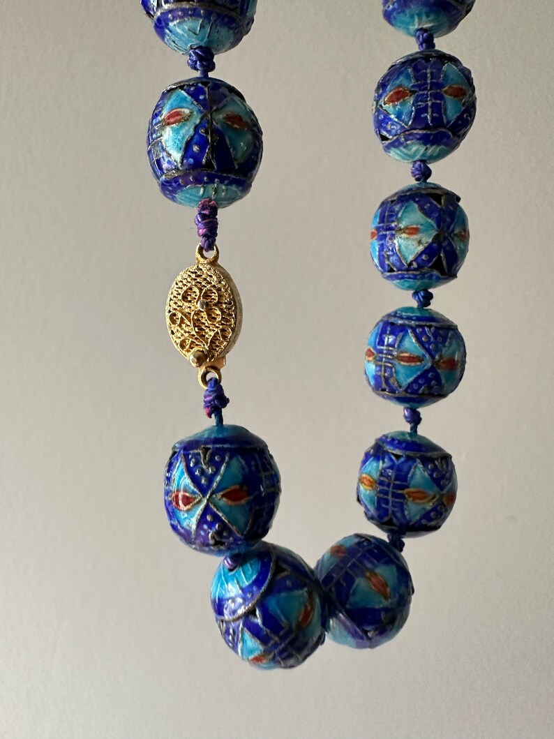 Puede incluir: Un collar azul y dorado con cuentas redondas. Las cuentas est&aacute;n decoradas con intrincados patrones en azul, blanco y rojo. El collar tiene un cierre dorado.