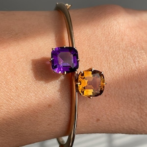 Könnte beinhalten: Ein goldenes Armreif-Armband mit einem violetten Amethyst und einem gelben Citrin.