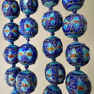 Puede incluir: Una hebra de cuentas de esmalte azul y blanco con intrincados patrones geom&eacute;tricos. Las cuentas est&aacute;n enhebradas en un cord&oacute;n y tienen un brillo met&aacute;lico.