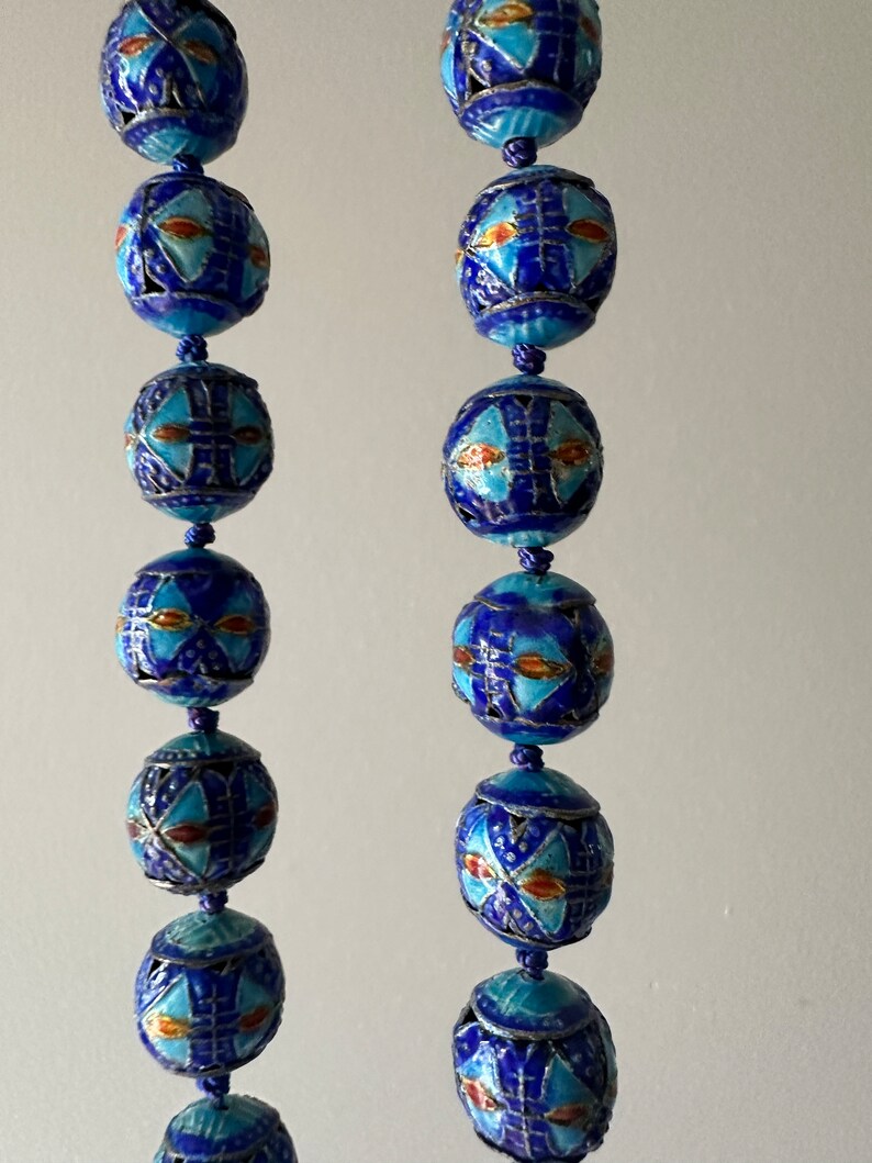 Puede incluir: Dos hileras de cuentas de esmalte azul y blanco con intrincados patrones geom&eacute;tricos. Las cuentas est&aacute;n enhebradas en un cord&oacute;n y tienen un acabado met&aacute;lico.