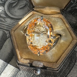 May include: A gold ring with a large, oval-shaped, orange gemstone. The ring is in a small, velvet-lined box with the inscription "Jewellers Toronto".