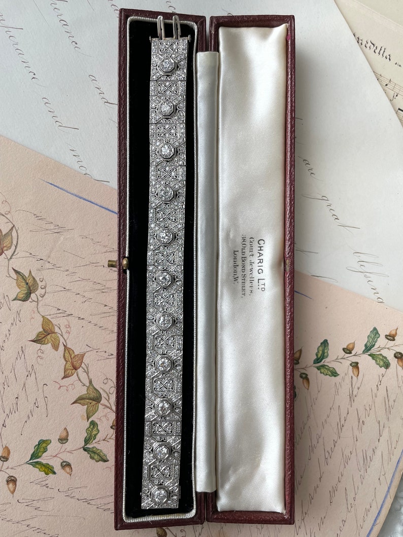 K&ouml;nnte beinhalten: Ein Diamantenarmband in einer roten Samtbox mit wei&szlig;er Satin-Auskleidung. Die Box ist mit "CHARIG LTD" beschriftet und hat die Adresse "38, OLD BOND STREET, LONDON, W."