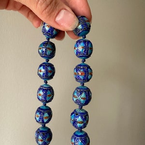 Puede incluir: Una larga hebra de cuentas de esmalte azul y blanco con intrincados patrones geom&eacute;tricos. Las cuentas son redondas y tienen un acabado brillante.