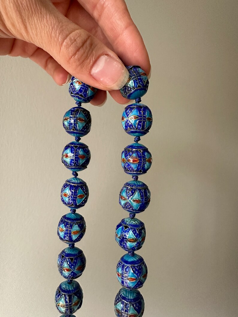 Puede incluir: Una larga hebra de cuentas de esmalte azul y blanco con intrincados patrones geom&eacute;tricos. Las cuentas son redondas y tienen un acabado brillante.