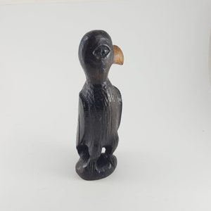 May include: A hand-carved wooden bird figurine with a black finish and a light brown beak. The bird is standing upright with its wings folded.
