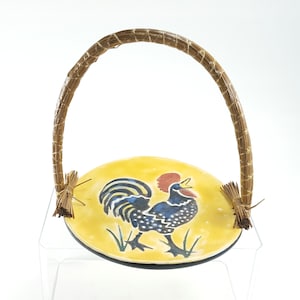May include: A yellow ceramic serving dish with a rooster design. The dish has a woven straw handle.