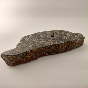 May include: A natural stone base with a dark gray and brown patterned surface. A brass screw is inserted into the stone. The stone has a unique, irregular shape, and is likely used as a decorative item or base.
