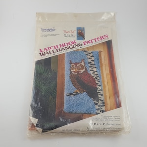 May include: A WonderArt latch hook wall hanging pattern kit in a clear plastic package. The kit features a design of a brown and red owl on a blue background. The finished size is 16 x 32 inches. The package includes the text "Tree Owl" and "LATCH HOOK WALL HANGING PATTERN".