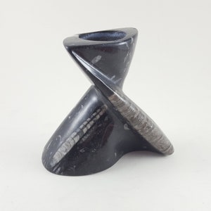 May include: A black and white fossilized ammonite candle holder. The holder is shaped like a spiral and has a smooth, polished finish.