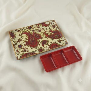May include: A rectangular tray featuring a cream-colored base with a detailed red and gold paisley pattern, accompanied by a smaller, solid red rectangular serving dish divided into three equal sections with a smooth, glossy finish.