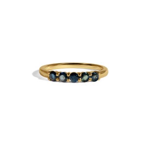 May include: A gold ring featuring five oval-cut, deep blue gemstones. The gemstones are set in a row across the top of the ring. The ring is set against a white background, highlighting the ring's design and color.