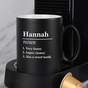 Pode incluir: Caneca de café preta com texto branco que diz "Hannah noun 1. Very funny 2. Super clumsy 3. Has a sweet tooth".