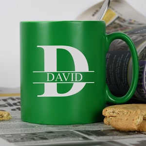 May include: A green ceramic mug with a white letter "D" and the name "DAVID" printed on it. The mug has a white handle and is sitting on a newspaper.