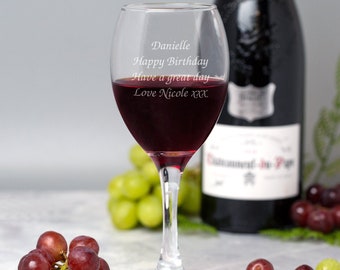 May include: A clear glass wine glass with a personalized message that reads "Danielle Happy Birthday Have a great day Love Nicole xxx". The glass is filled with red wine and is sitting on a table with grapes.