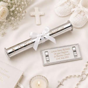 Peut inclure: Un porte-certificat cylindrique argenté gravé avec le texte On Your Baptism, orné d'un nœud en ruban de satin blanc. À côté se trouve une plaque rectangulaire argentée gravée avec Lorcan James Richards, On your Baptism, St Martins Chruch, 23rd July 2026.