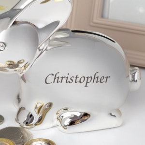 May include: A silver bunny piggy bank with a slot on the back for coins. The piggy bank is personalized with the name "Christopher".