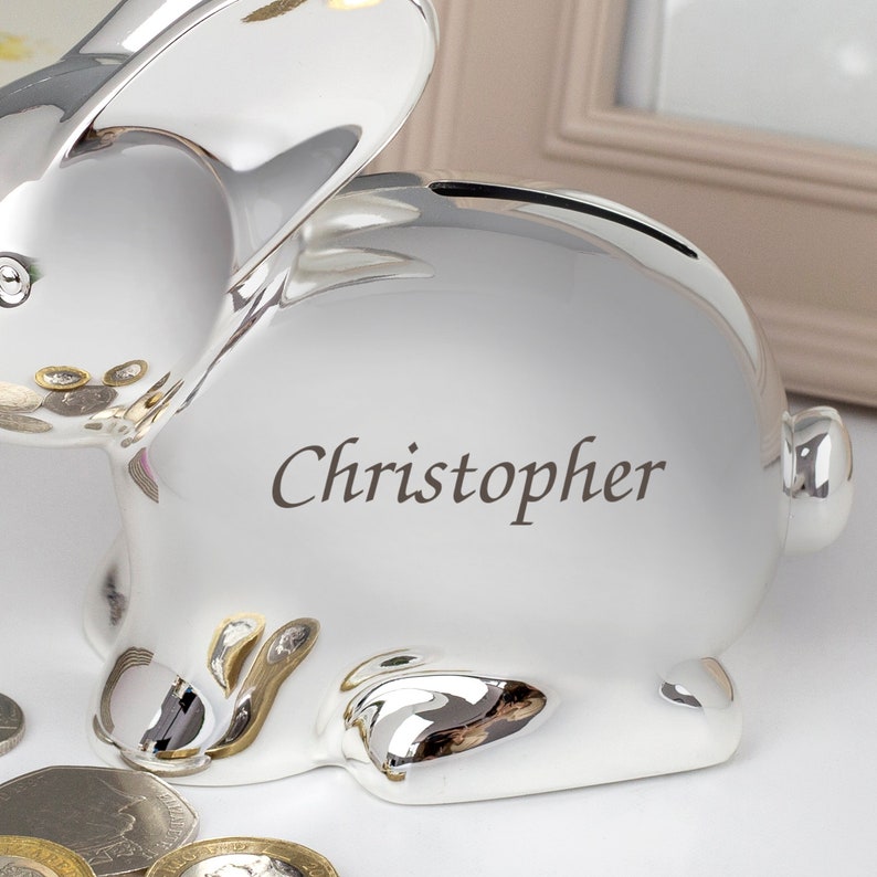 May include: A silver bunny piggy bank with a slot on the back for coins. The piggy bank is personalized with the name "Christopher".