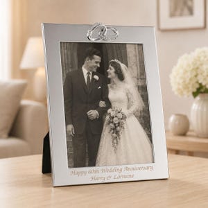 May include: A silver-toned rectangular photo frame featuring two interlocking rings at the top. The frame displays a black and white wedding photograph and is engraved with the text "Happy 60th Wedding Anniversary" and "Harry & Lorraine" at the bottom.