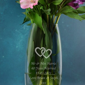 May include: A clear glass vase with two intertwined hearts etched into the front. The vase is filled with pink and purple flowers. The text "Mr & Mrs Harris 40 Years Married 15.03.2021 Love Brian & Steph xxx" is etched into the vase.