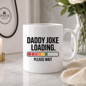 Peut inclure: Un mug en céramique blanc avec le texte noir DADDY JOKE LOADING. et PLEASE WAIT. Sous le texte se trouve un graphique de barre de chargement horizontale avec des segments rouges, orange, jaunes et verts sur un fond blanc.