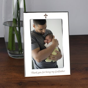 May include: Silver photo frame with a cross on top and the inscription "Thank you for being my Godfather". A photo of a man holding a baby is inside the frame.