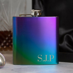 May include: A stainless steel hip flask with a rainbow iridescent finish. The flask has a silver cap and a personalised inscription that reads "S.J.P."