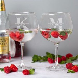 May include: Two clear glass gin glasses with the names "Kelly" and "Matthew" etched on them. The glasses are filled with a clear liquid and raspberries.