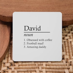 May include: White coaster with black text that reads "David noun 1. Obsessed with coffee 2. Football mad! 3. Amazing daddy"