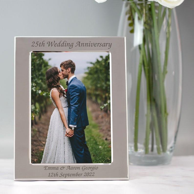 May include: Silver photo frame with a picture of a couple kissing. The frame is engraved with "25th Wedding Anniversary", "Emma & Aaron Georgio", and "12th September 2022".