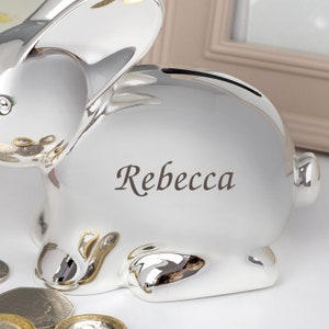May include: Silver bunny piggy bank with a slot on the back for coins. The piggy bank is personalized with the name "Rebecca".