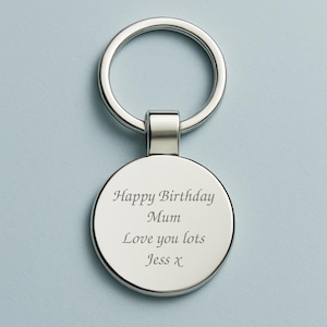 以下が含まれることがあります： 丸いペンダントが付いたシルバーカラーのキーホルダー。ペンダントには「Happy Birthday Mum Love you lots Jess x」と刻印されています。キーホルダーには鍵を取り付けるためのリングが付いています。