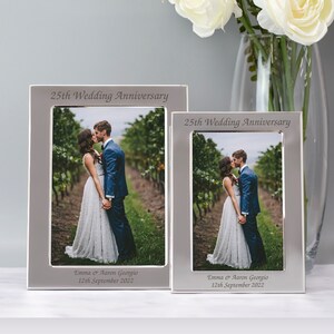 May include: Two silver picture frames with a white mat and a black and white photo of a couple kissing. The frames are engraved with "25th Wedding Anniversary" and "Emma & Aaron Georgio 12th September 2022".