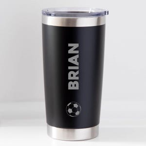 May include: Black insulated tumbler with a silver rim and lid. The name "BRIAN" is vertically printed in silver, along with a soccer ball graphic. The tumbler is designed to keep beverages hot or cold.