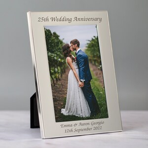 May include: Silver photo frame with a picture of a couple kissing. The frame is engraved with "25th Wedding Anniversary", "Emma & Aaron Georgio", and "12th September 2022".