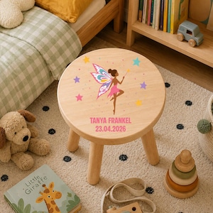 May include: A round wooden stool featuring a printed graphic of a fairy with colourful wings, surrounded by small stars. The text "TANYA FRANKEL" and "23.04.2026" is printed in pink below the fairy illustration on the light wood surface.
