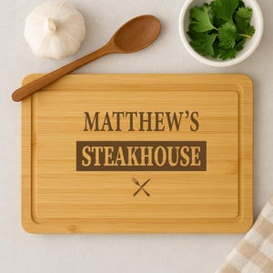Può includere: Un tagliere in legno marrone con il testo "Matthew's Steakhouse" inciso su di esso. Il tagliere ha un incavo attorno al bordo e un piccolo simbolo di coltello e forchetta al centro inferiore.