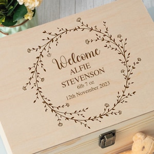 Op de afbeelding: Een houten bewaardoos met een gegraveerd ontwerp van een bloemenkrans op de deksel. De doos is gepersonaliseerd met de tekst "Welcome Alfie Stevenson 6lb 7oz 12th November 2023".