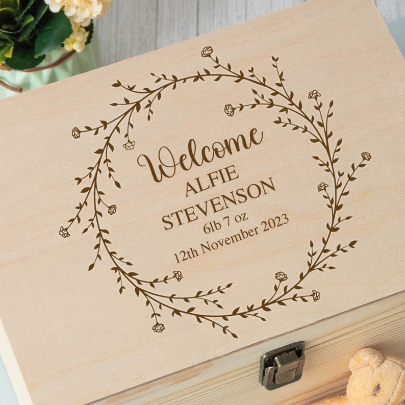 Op de afbeelding: Een houten bewaardoos met een gegraveerd ontwerp van een bloemenkrans op de deksel. De doos is gepersonaliseerd met de tekst "Welcome Alfie Stevenson 6lb 7oz 12th November 2023".
