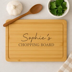 Op de afbeelding: Een lichtbruin houten snijplank met de tekst "Sophie's Chopping Board" erop gegraveerd.