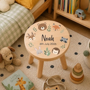 Puede incluir: Un taburete redondo de madera con acabado de veta clara y un diseño impreso de varios animales del bosque, incluyendo un oso, zorro, ciervo, mapache, erizo y conejo. El centro muestra el nombre Noah y la fecha 6th July 2026.