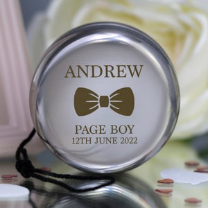 Könnte beinhalten: Silbernes Jojo mit schwarzem Band. Das Jojo hat eine personalisierte Inschrift mit dem Text "ANDREW PAGE BOY 12TH JUNE 2022" und eine braune Fliege.