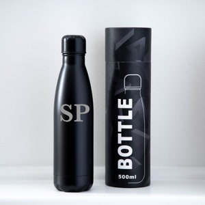 May include: Black insulated water bottle with silver initials "SP". Beside it is a black cylindrical box with the word "BOTTLE" and a bottle outline. The box also has "500ml" printed on it. The bottle is designed to hold 500ml of liquid.