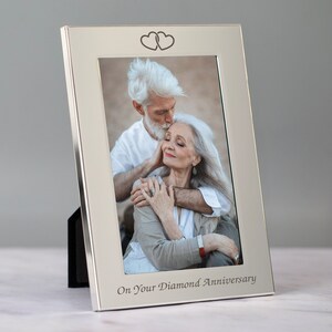 Op de afbeelding: Zilveren fotolijst met twee in elkaar verweven harten gegraveerd aan de bovenkant. De lijst bevat een foto van een ouder koppel dat elkaar omarmt. De onderkant van de lijst is gegraveerd met de tekst "On Your Diamond Anniversary".