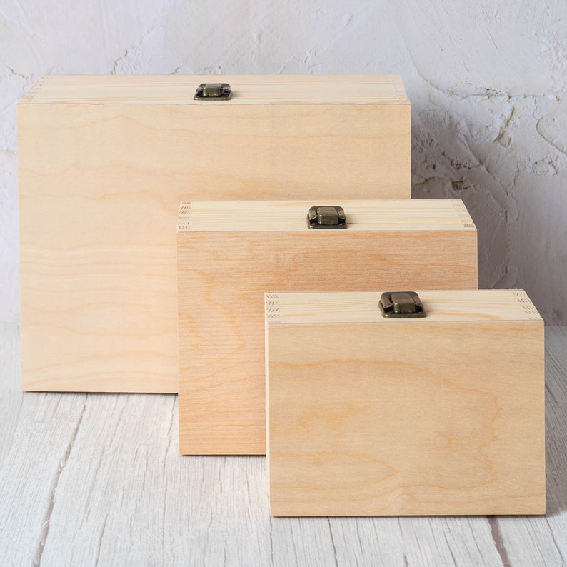Op de afbeelding: Drie houten dozen in verschillende maten, elk met een messing sluiting. De dozen zijn gemaakt van licht hout en zijn gerangschikt in aflopende volgorde van grootte.