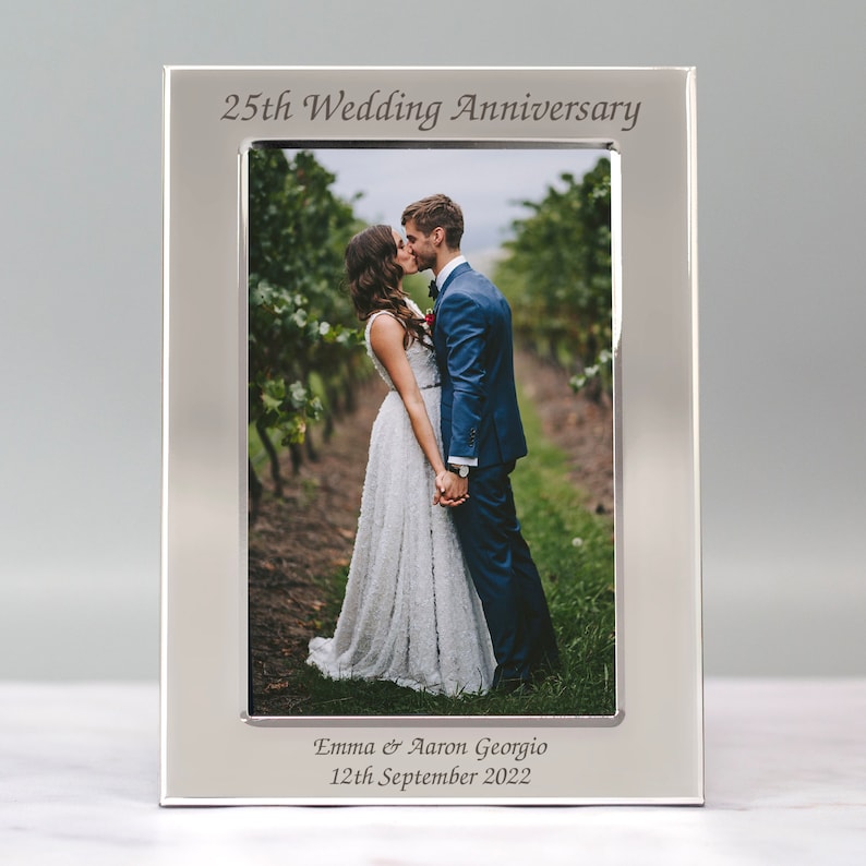 May include: Silver photo frame with a picture of a couple kissing. The frame is engraved with "25th Wedding Anniversary", "Emma & Aaron Georgio", and "12th September 2022".