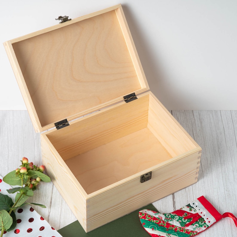 Op de afbeelding: Een houten doos met een scharnierend deksel, open om het lege interieur te laten zien. De doos is gemaakt van licht hout en heeft een natuurlijke afwerking.