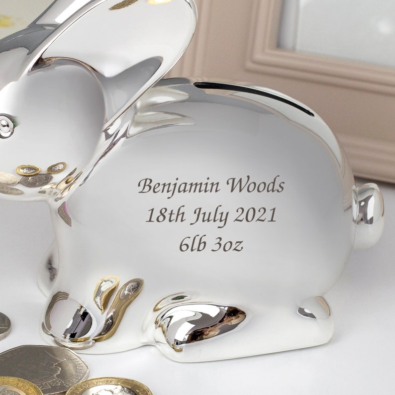 May include: Silver bunny shaped piggy bank with a personalized inscription that reads "Benjamin Woods 18th July 2021 6lb 3oz".