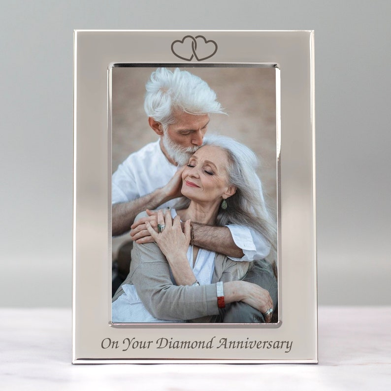 Op de afbeelding: Zilveren fotolijst met een foto van een ouder koppel dat elkaar omhelst. De lijst heeft bovenaan twee in elkaar verweven harten en onderaan de inscriptie "On Your Diamond Anniversary".