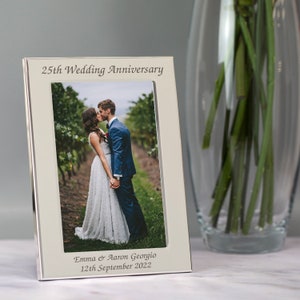 May include: Silver photo frame with a white mat and a picture of a couple kissing. The frame has the text "25th Wedding Anniversary" at the top and "Emma & Aaron Georgio 12th September 2022" at the bottom.