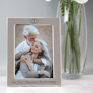 Op de afbeelding: Zilveren fotolijst met een stel op een foto. De lijst heeft twee gegraveerde harten bovenaan en de woorden "On Your Diamond Anniversary" gegraveerd onderaan.